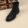 Women's black ankle motorcycle boot with rubber sole, featuring a knit cuff, against a London-themed background.