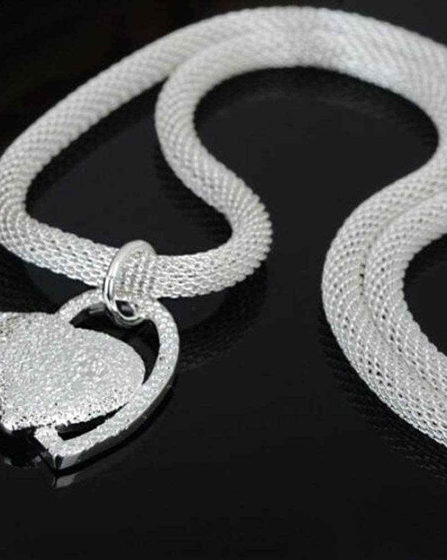 Silver net style heart necklace with fine jewelry detailing on a dark background.