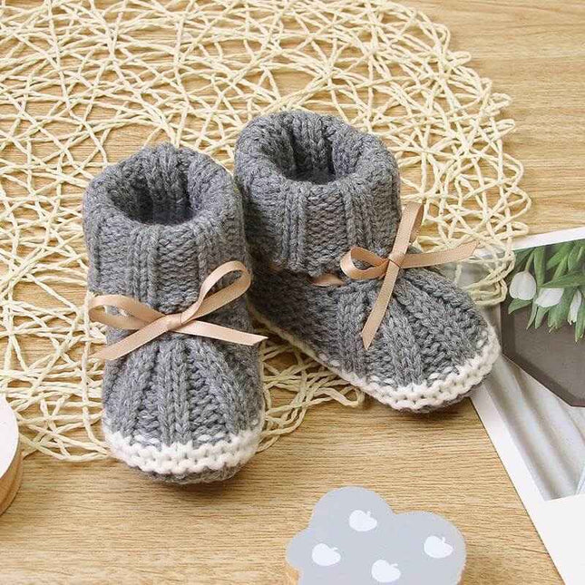 Fashionable and lightweight toddler shoes in gray with ribbon bows on a woven mat.