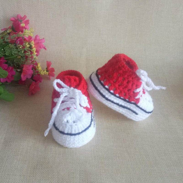 Hand-knitted baby bootees in red and white with floral background.