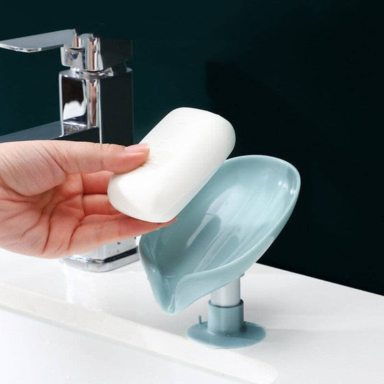 Soap dish with double drain holes, in a sleek Leaf design, beside a bathroom sink faucet.