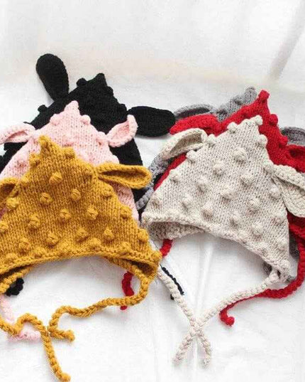 Hand knitted baby hats with cartoon ears and colorful woven balls.