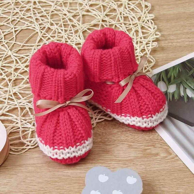 Fashionable and lightweight toddler shoes in red with white trim on a wooden surface.