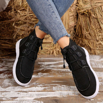 Round toe flat sneakers with lace-up design for women, black color, worn with jeans.