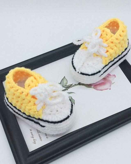 Hand-knitted baby bootees in yellow and white on a decorative tray.