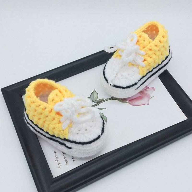 Hand-knitted baby bootees in yellow and white on a decorative tray.